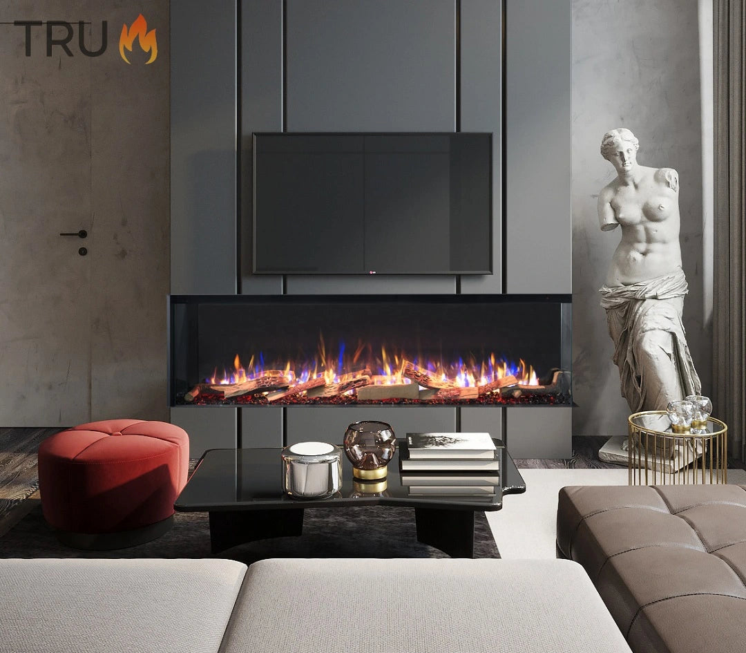An electric fireplace with a 3-sided media wall design, featuring multicolored flames, situated in a modern living room setting with a statue, couch, and coffee table.